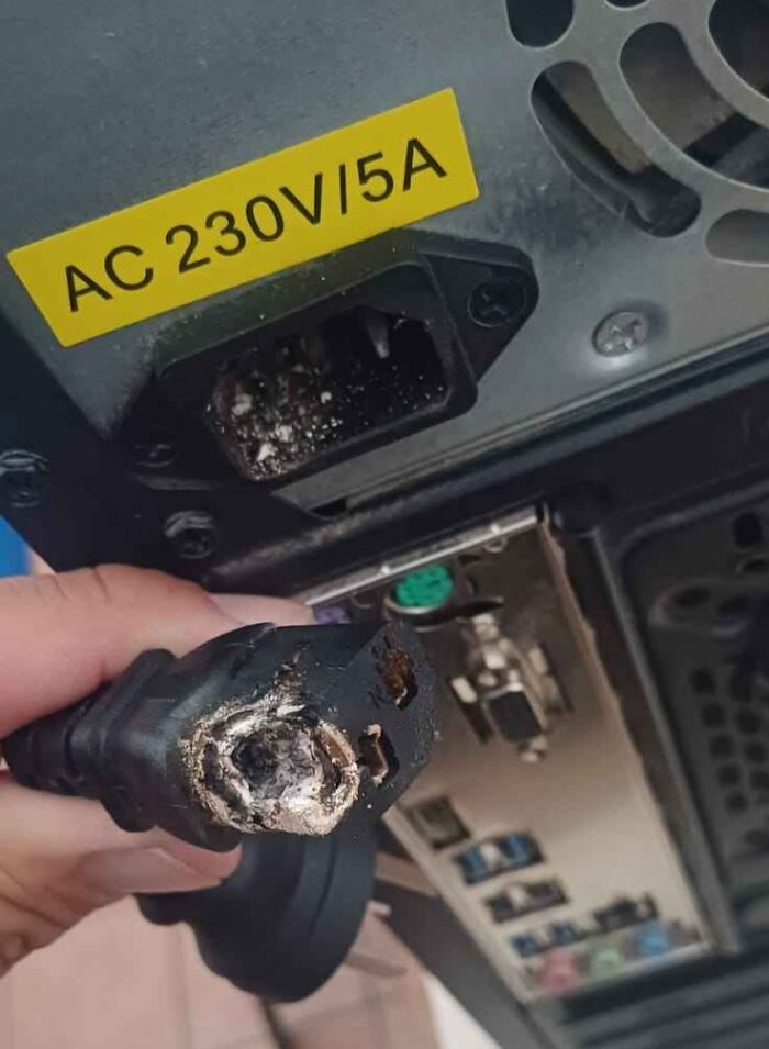 Burnt power plug held near damaged AC 230V 5A socket showing electronics handled the wrong way.