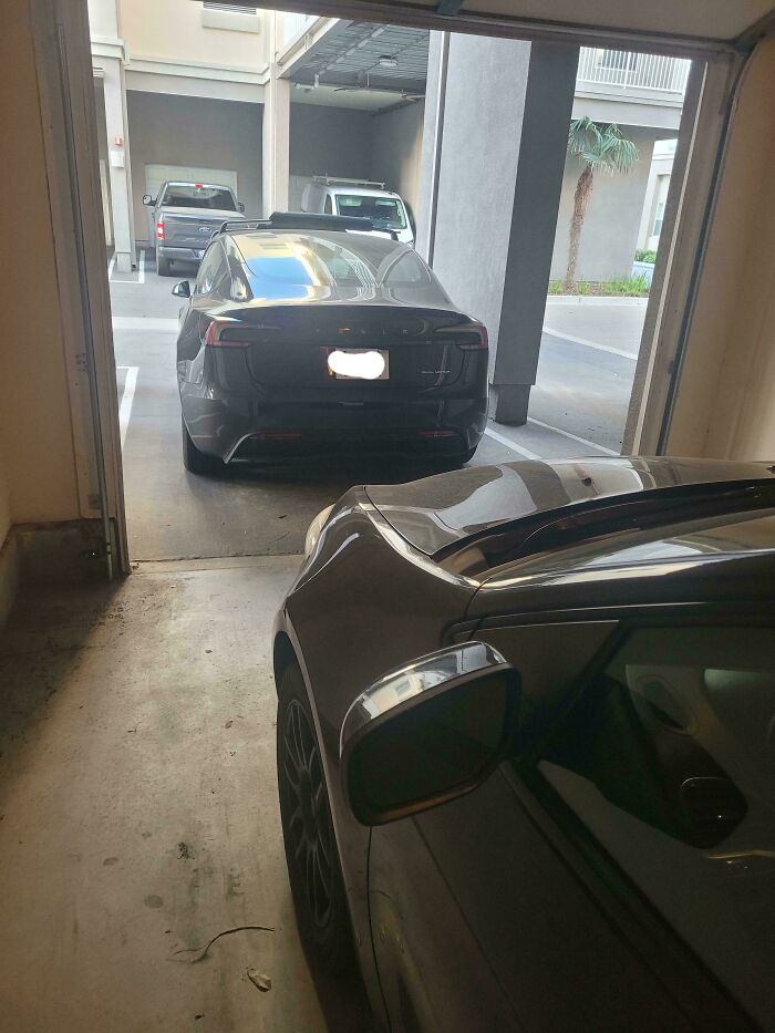 Black car blocking garage exit, causing mild infuriation and testing patience in a tight parking space.