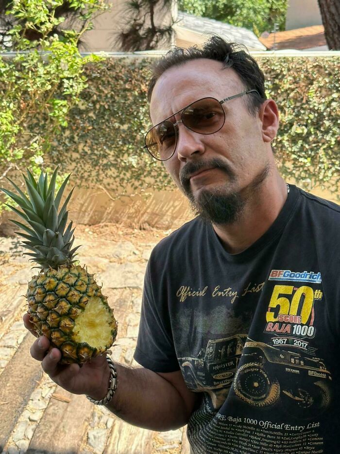 Man holding a pineapple with a bite taken out, showcasing a mildly infuriating thing that tested patience outdoors.