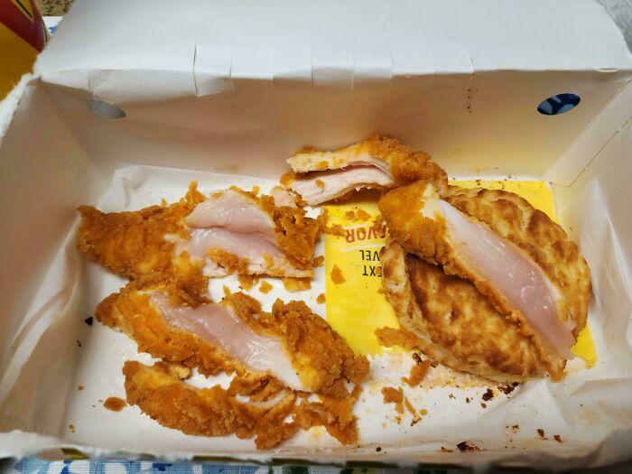 Partially cooked fried chicken pieces in a takeout box showing raw, undercooked meat, mildly infuriating food fail.
