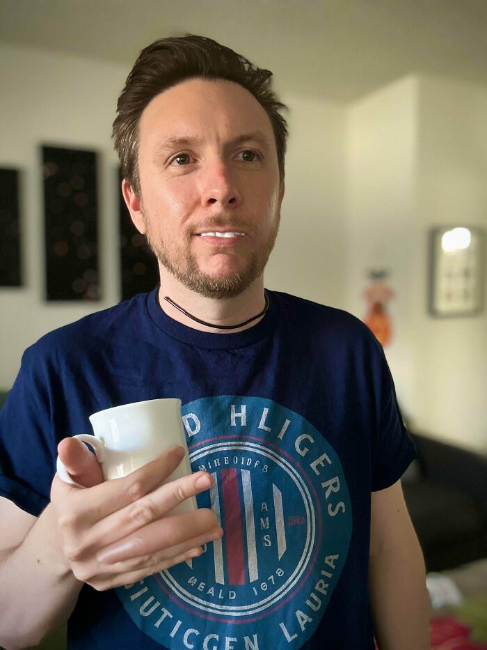 Man holding a white mug indoors, wearing a blue shirt, representing creative Halloween costume ideas for men.