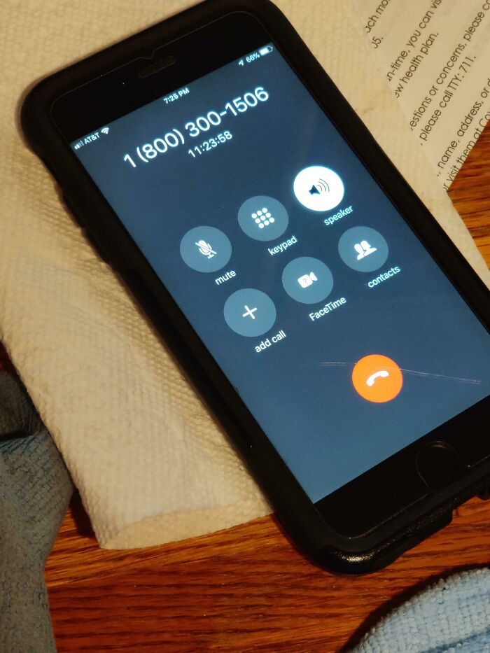 Smartphone on a wooden table with a call in progress to a healthcare number, highlighting American healthcare challenges.