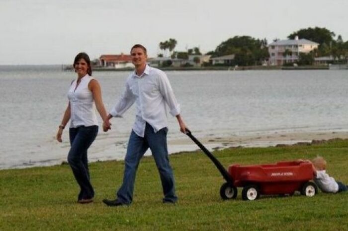Pareja caminando en la playa tirando un carrito rojo con un niño sentado de forma incómoda familia fotos icónicas.