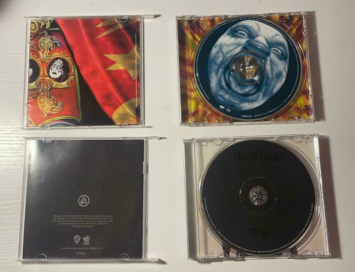 Four different CD cases laid open on a white surface, showcasing album art and discs causing mild infuriation.