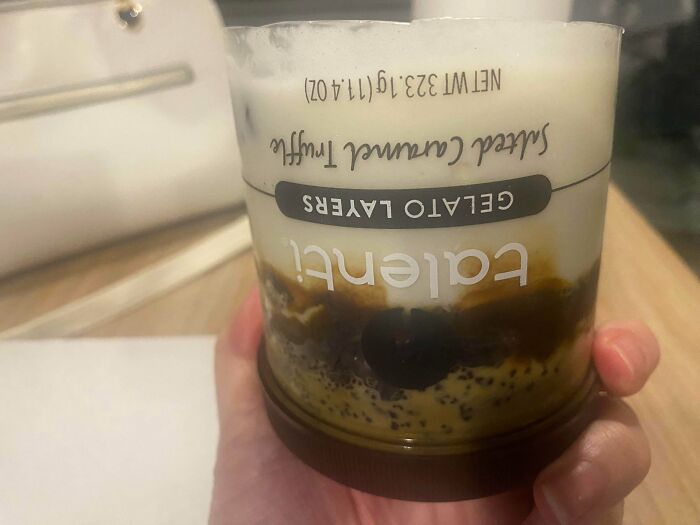 Hand holding a dessert cup with upside-down label, showing mildly infuriating design that tests patience.