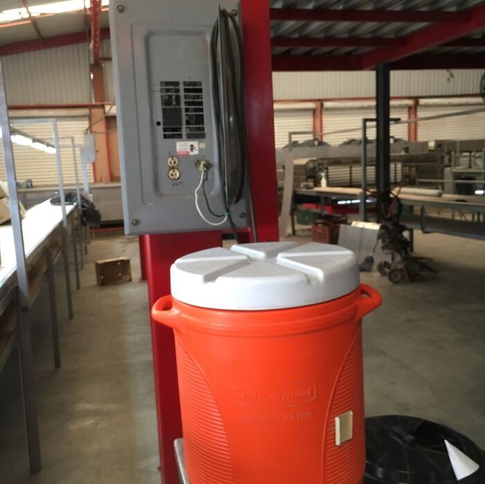 Orange water cooler placed next to an electrical panel with exposed wiring, illustrating improper electronics handling.