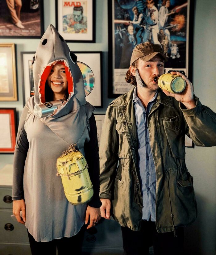 Couple wearing creative Halloween costumes with a shark outfit and themed accessories in a vintage-decorated room.