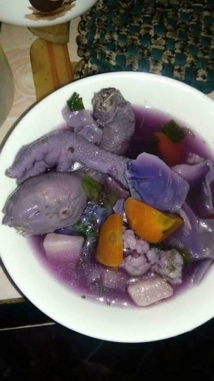 Bowl of unholy food with purple broth, chicken feet, and mixed vegetables looking anything but appetizing