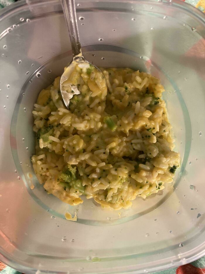 Unholy food pic of soggy rice and broccoli mixture in a plastic container with a spoon, looking unappetizing.