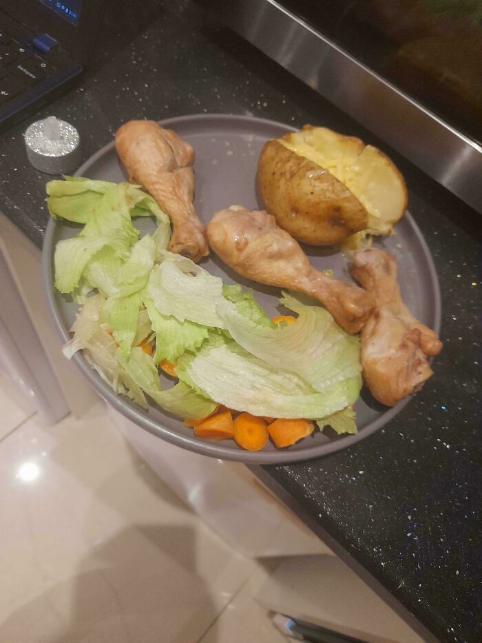 Plate with unholy food pics showing boiled chicken drumsticks, a baked potato, and wilted lettuce with carrot pieces.