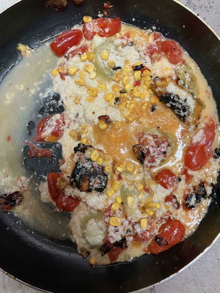 Burnt and unappetizing food with melted cheese, corn, tomatoes, and charred bits in a frying pan, unholy food pics.