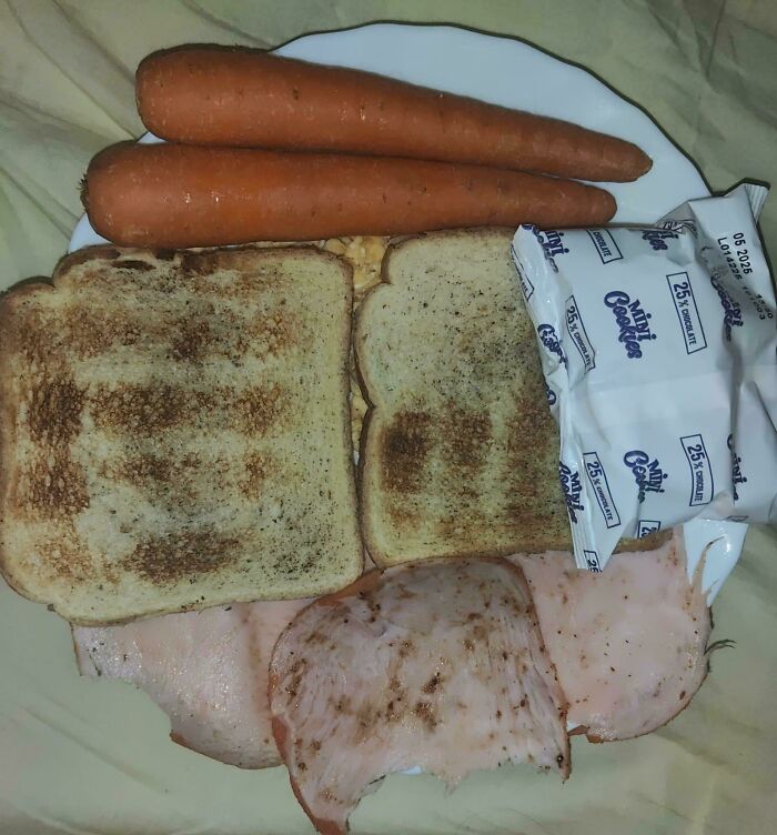 Unholy food plate with toasted bread, sliced deli meat, whole carrots, and packaged cookies in unappetizing arrangement.