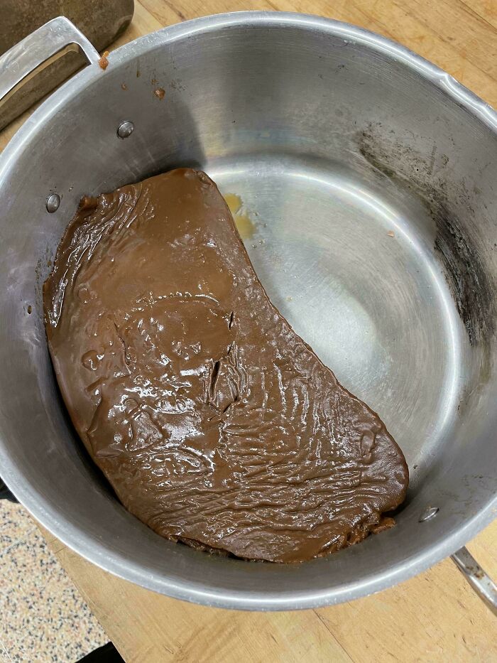 Unholy food pic showing a greasy, unappetizing brown substance in a metal pot on a wooden surface.