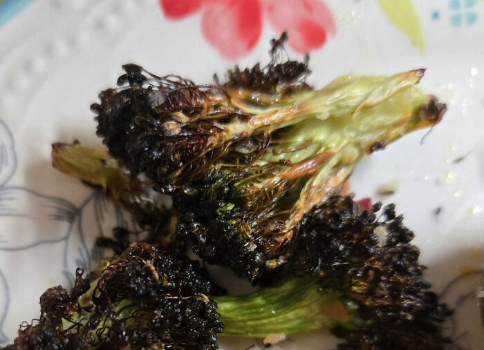 Burnt and unappetizing broccoli pieces on a floral plate, showcasing unholy food pics with an unpleasant appearance.