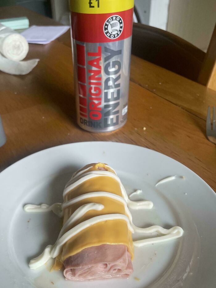 Unholy food pic of a rolled ham slice topped with cheese and mayonnaise on a white plate with an energy drink can nearby.
