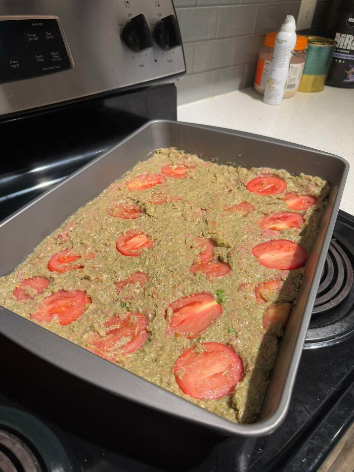 Baking pan with unappetizing food mixture topped with tomato slices resembling unholy food pics.