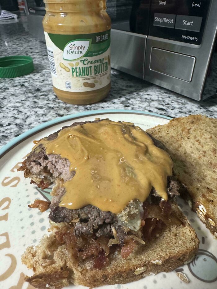 Unholy food pic showing a burger with peanut butter spread on the patty served on whole grain bread.