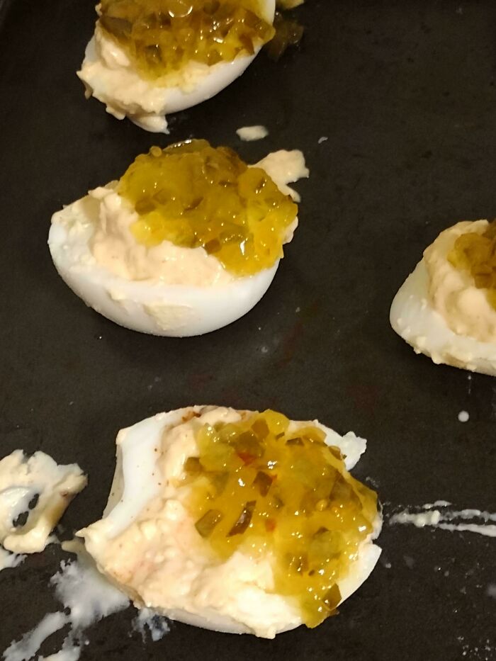 Unholy food pics showing deviled eggs with yellow relish on a dark surface, looking unappetizing and messy.