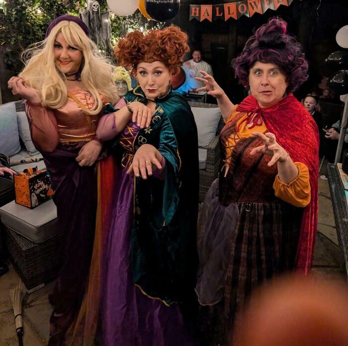 Three women wearing creative Halloween costumes inspired by witches at a festive Halloween party with decorations.