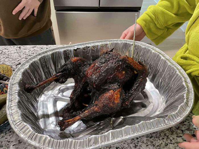 Burnt chicken in a foil tray with a cooking thermometer, an unholy food pic that looks unappetizing and overcooked.