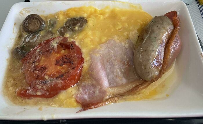 Unholy food plate with scrambled eggs, grilled tomato, mushrooms, bacon, and sausage that looks anything but appetizing