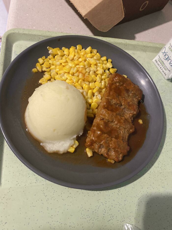 Plate of mashed potatoes, corn, and meat with gravy on a tray, an unholy food pic that looks unappetizing.