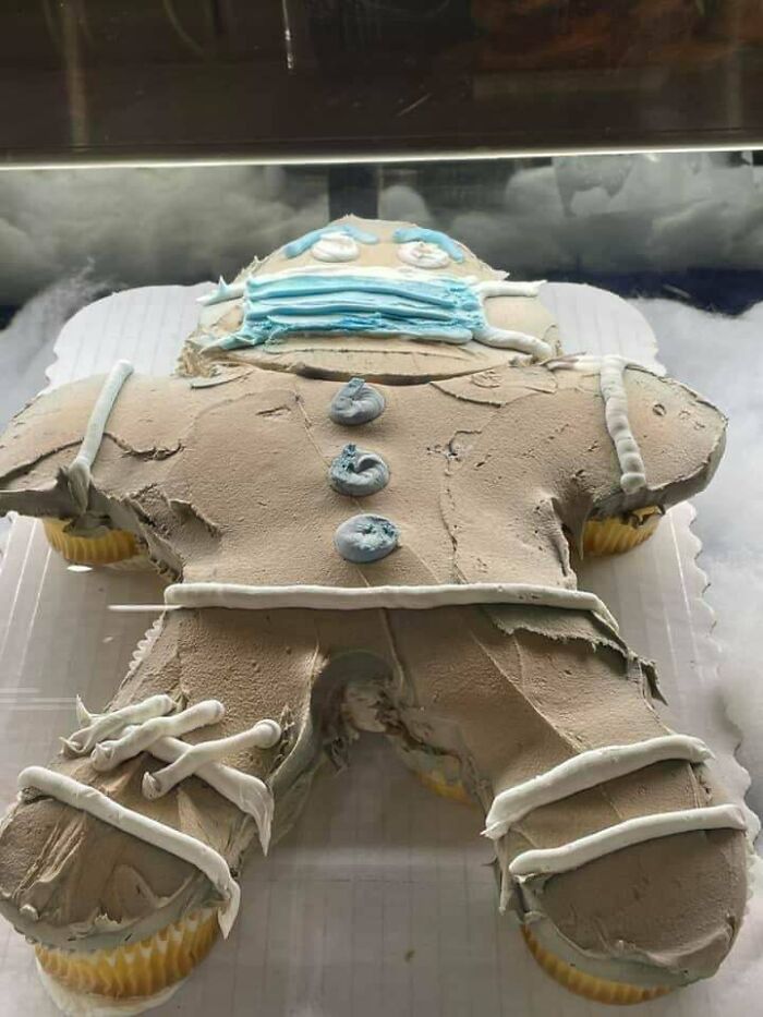 Unholy food pic of a distorted gingerbread man cupcake with uneven frosting and a blue face mask decoration.