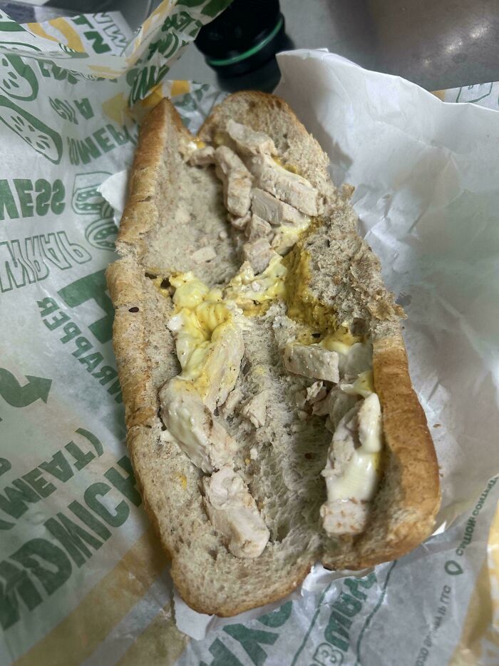 Unholy food pic of a poorly made chicken sandwich with sparse filling and messy sauce on whole wheat bread.