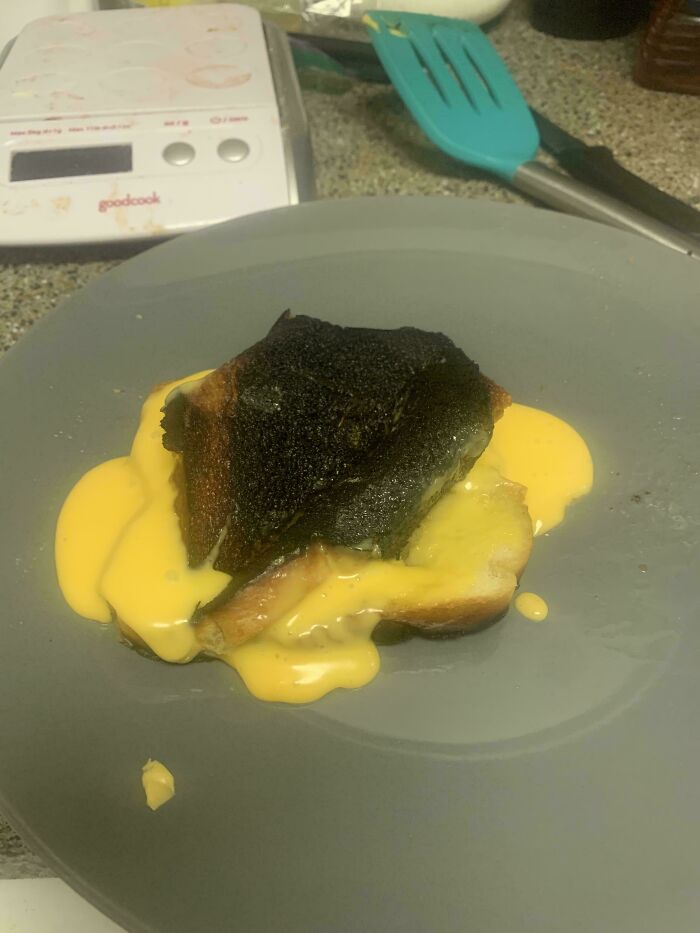 Burnt sandwich with melted cheese on a plate, one of the unholy food pics that look anything but appetizing.