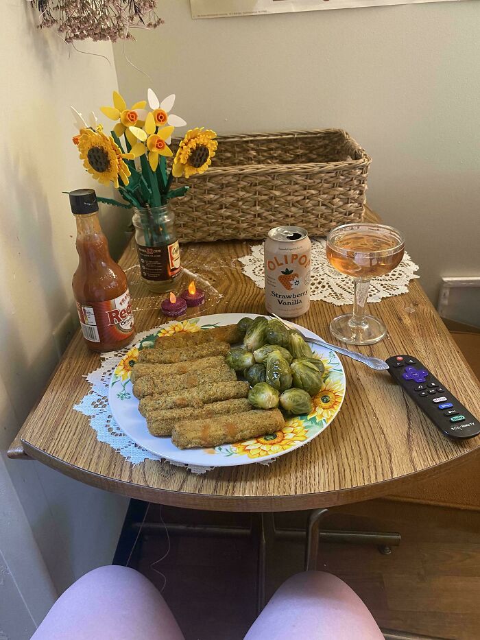 Unappetizing food plate with fried sticks and Brussels sprouts on a wooden table with drink and hot sauce nearby.