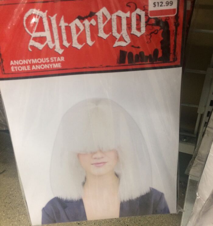 Off-brand Halloween costume wig with a large white bob covering model's eyes, displayed in packaging on store shelf.