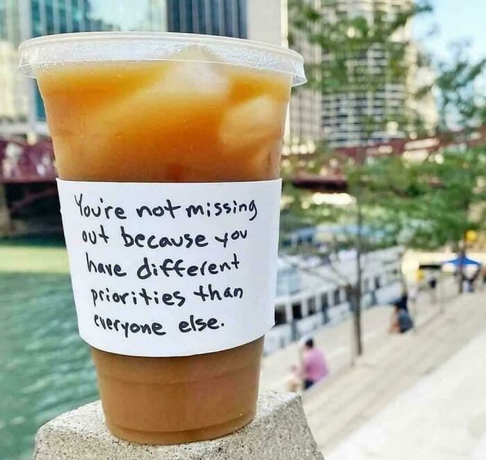 Iced coffee cup with a handwritten note about different priorities, reflecting simple living values by the riverside.