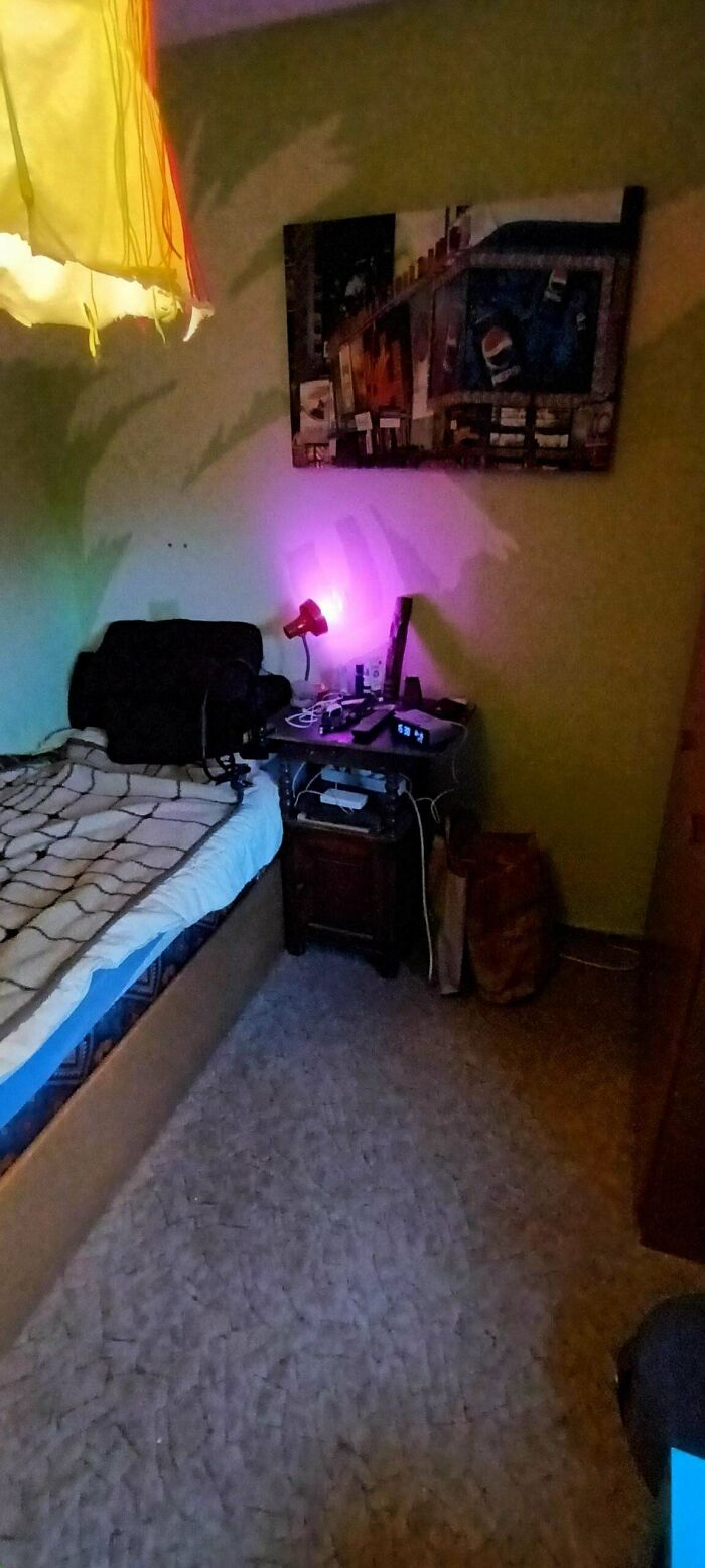 Minimalist bedroom corner with a simple bed, small nightstand, and soft colored lighting showcasing simple living.