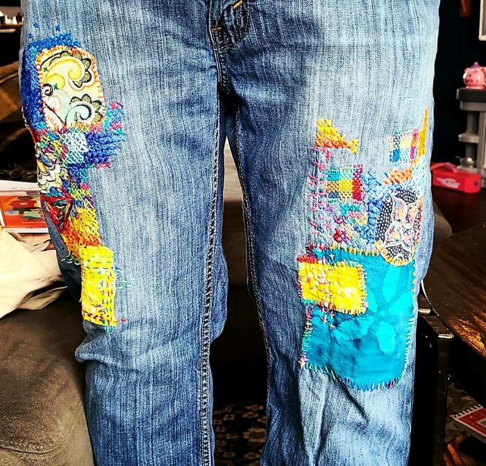 Denim jeans with colorful patchwork repairs, showcasing simple living through mindful and creative clothing reuse.