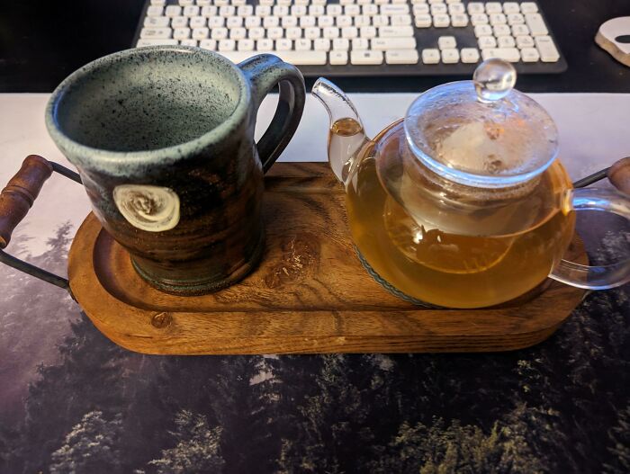 Ceramic mug and glass teapot with tea on a wooden tray, illustrating simple living and minimalistic lifestyle.