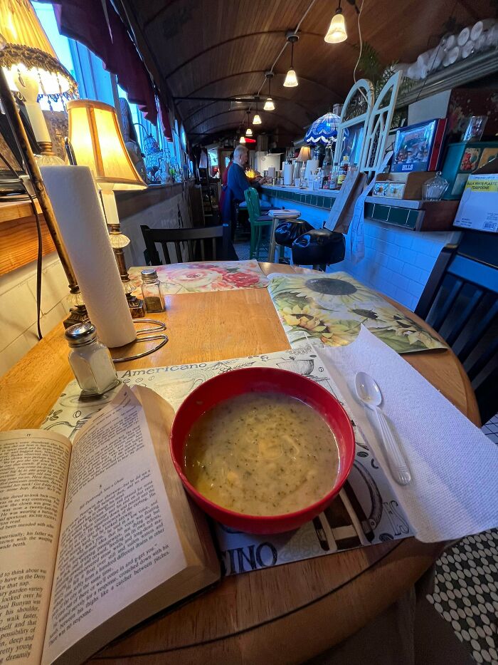 Cozy simple living scene with a bowl of soup, open book, and rustic diner interior emphasizing having less.