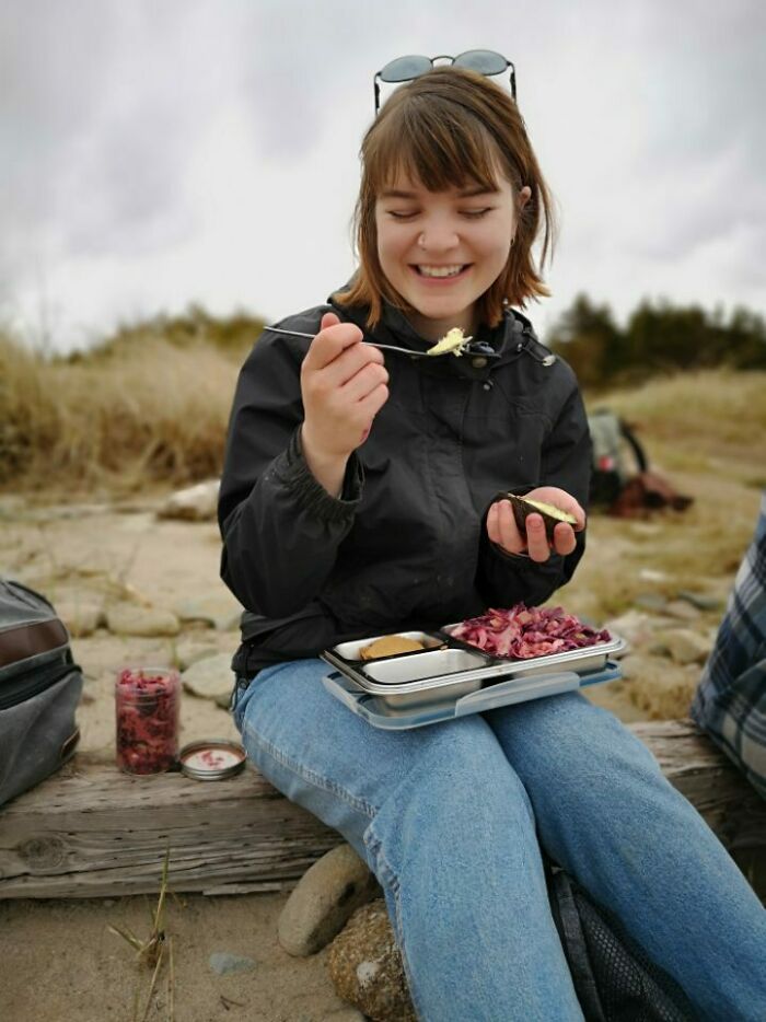 Young woman enjoying a simple living lunch outdoors, sitting on a log with minimal items and natural surroundings.
