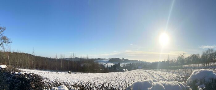 Snow-covered rural landscape under a clear blue sky with the sun shining, evoking simple living and minimalism.