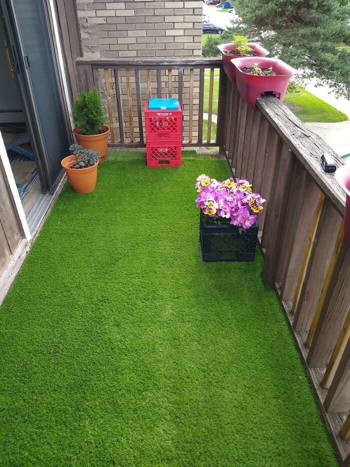 Balcony with simple living decor featuring artificial grass, potted plants, and minimal furniture for a cozy outdoor space.