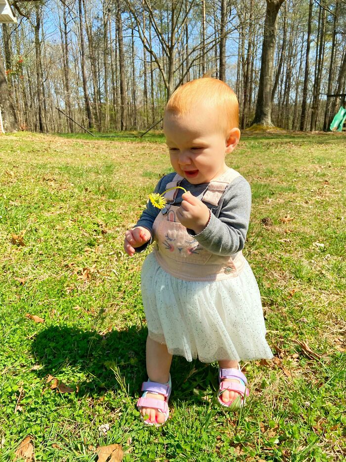 Toddler exploring nature outdoors, holding a small flower, embodying the simple living lifestyle in a peaceful grassy area.