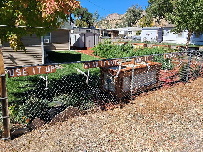 Fence with antlers and simple living signs encouraging use, wear, make, or do without, near modest homes and garden.