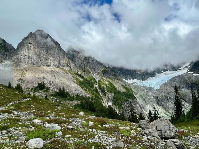 Mountain landscape with rocky terrain and evergreen trees under a cloudy sky, reflecting simple living and nature's beauty.