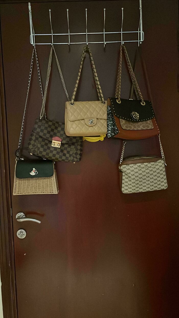 Five designer handbags hanging neatly on a rack against a door, illustrating simple living and minimalist organization.