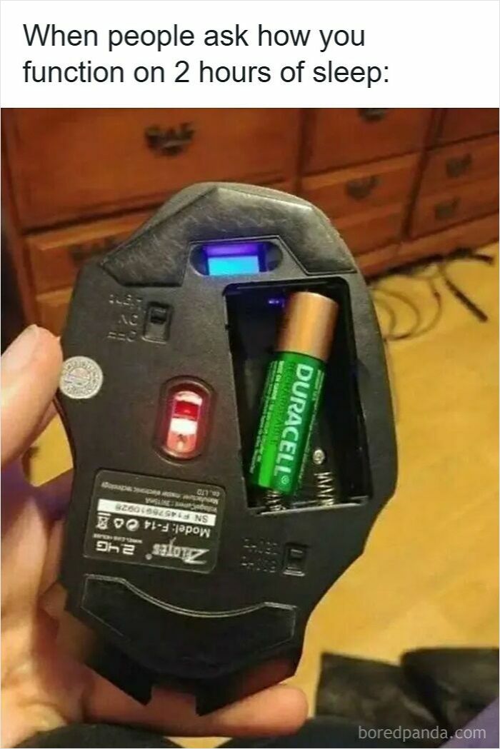 Hand holding a computer mouse with one battery missing, illustrating low energy and funny insomnia memes.