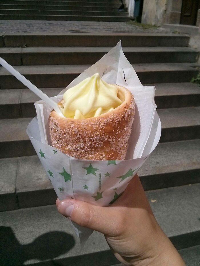 Hand holding a sugar-coated pastry cone filled with soft-serve ice cream, an uncommon food tourists expect in some countries.