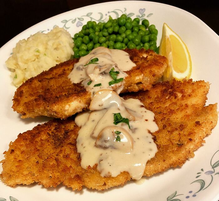 Breaded fish fillets with mushroom sauce, mashed potatoes, and peas on a plate, illustrating unpopular foods in some countries.