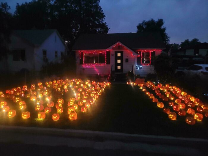 Yard filled with glowing jack-o'-lanterns and house decorated with red Halloween lights for outdoor Halloween decorations.