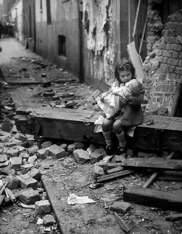Young girl sitting amid rubble holding a doll, a powerful photo representing fascinating photos and stories that see the world differently.