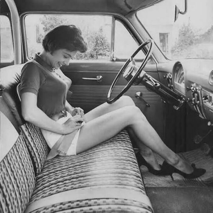 Black and white photo of woman fastening seatbelt in vintage car, illustrating fascinating photos and stories about the world.