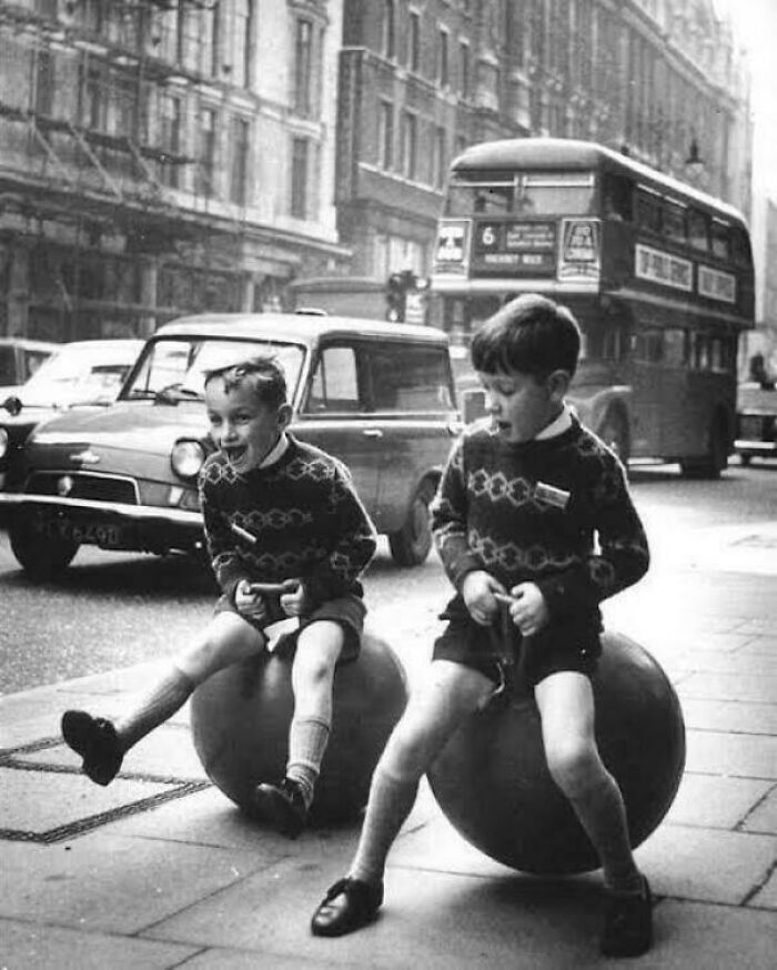 Two boys in vintage sweaters playing with bouncing balls on a city street, capturing fascinating photos and moments.